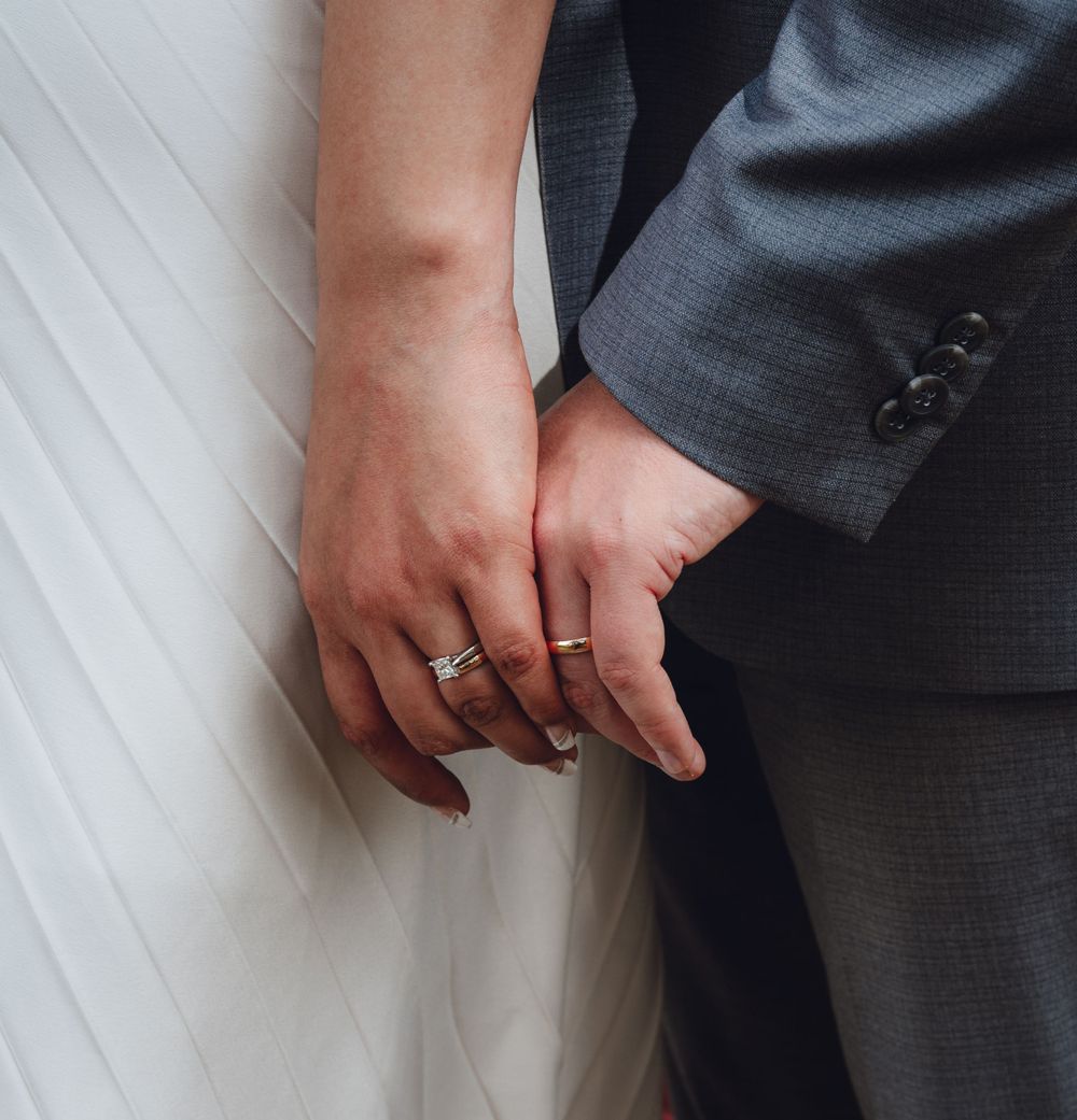 Close-up of hands showing wedding rings against white dress fabric.