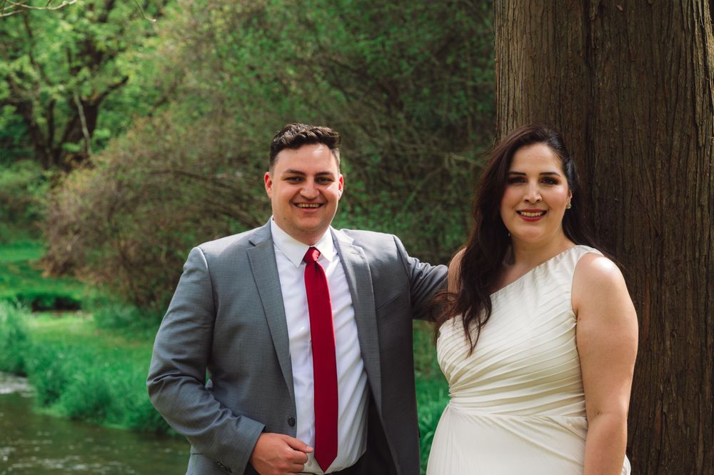 Wedding couple poses together in front of tall trees in a natural outdoor setting.