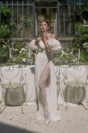 Elegant white vintage chairs arranged in a garden setting with a figure in a flowing white dress.
