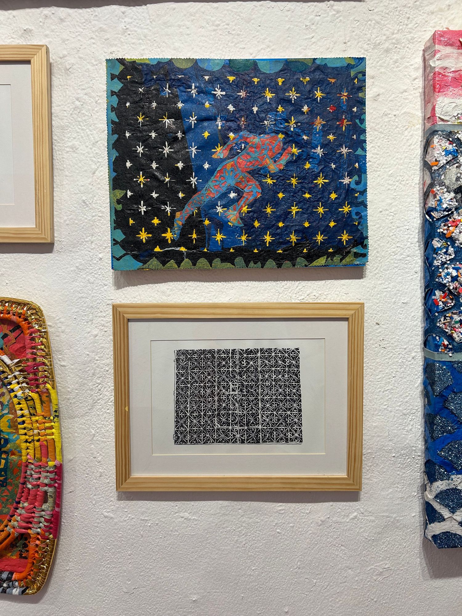 Colorful artwork on gallery walls featuring a figure against a starry background and a framed abstract pattern below.