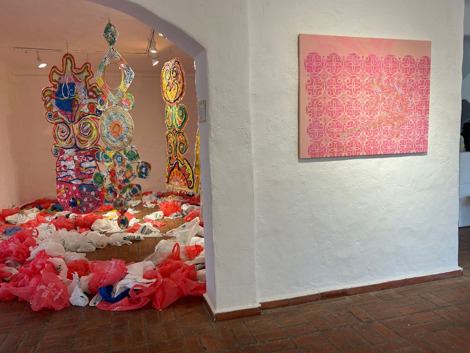 Gallery view showing colorful sculptural installation and pink wall art in arched doorway.