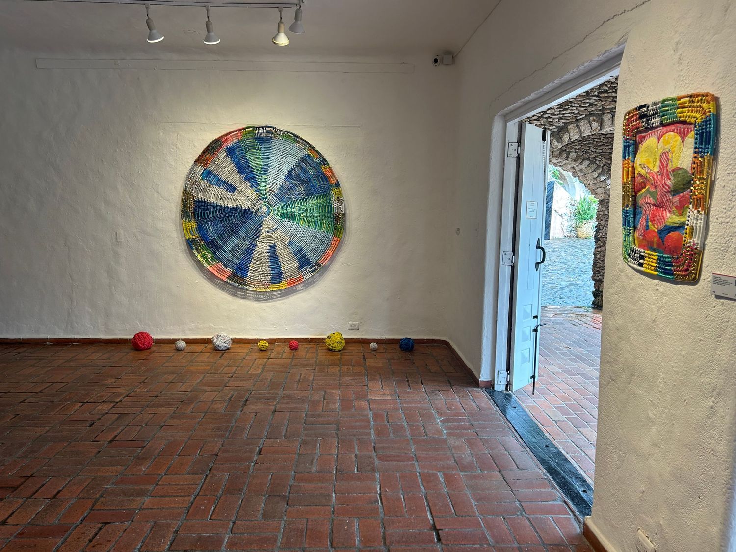 Circular blue starburst artwork mounted on white wall with brick flooring and doorway visible.