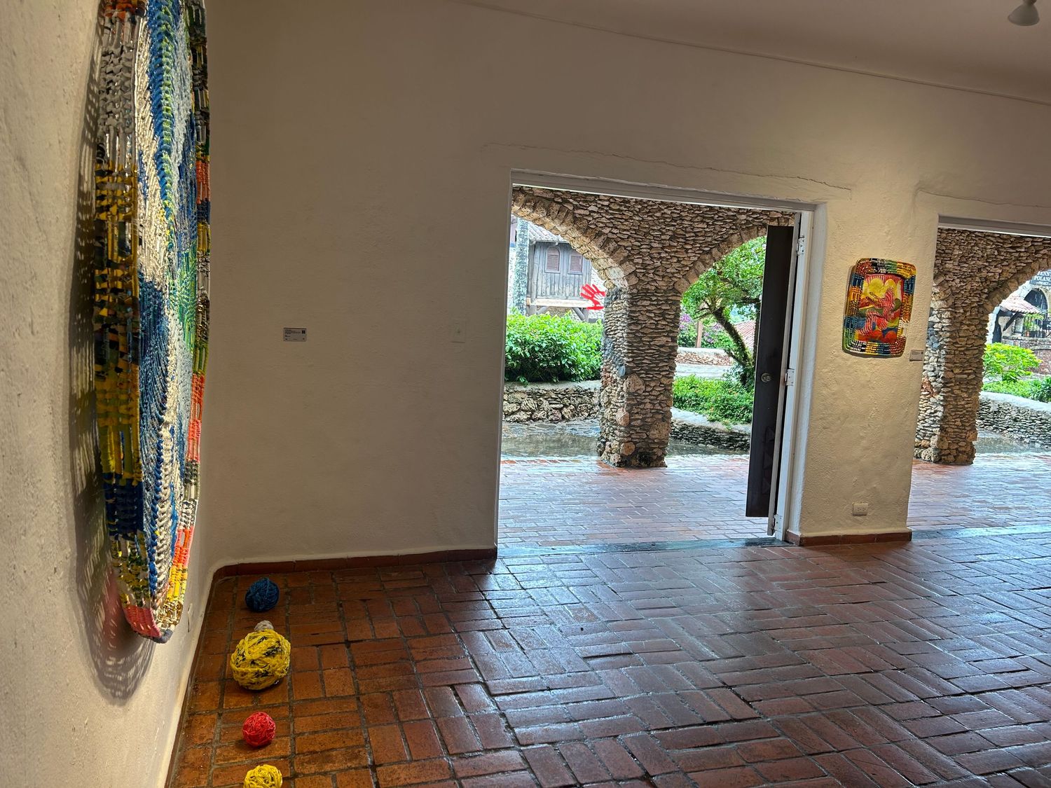 Modern art gallery space with tall abstract painting and yellow sculptures on brick floor.