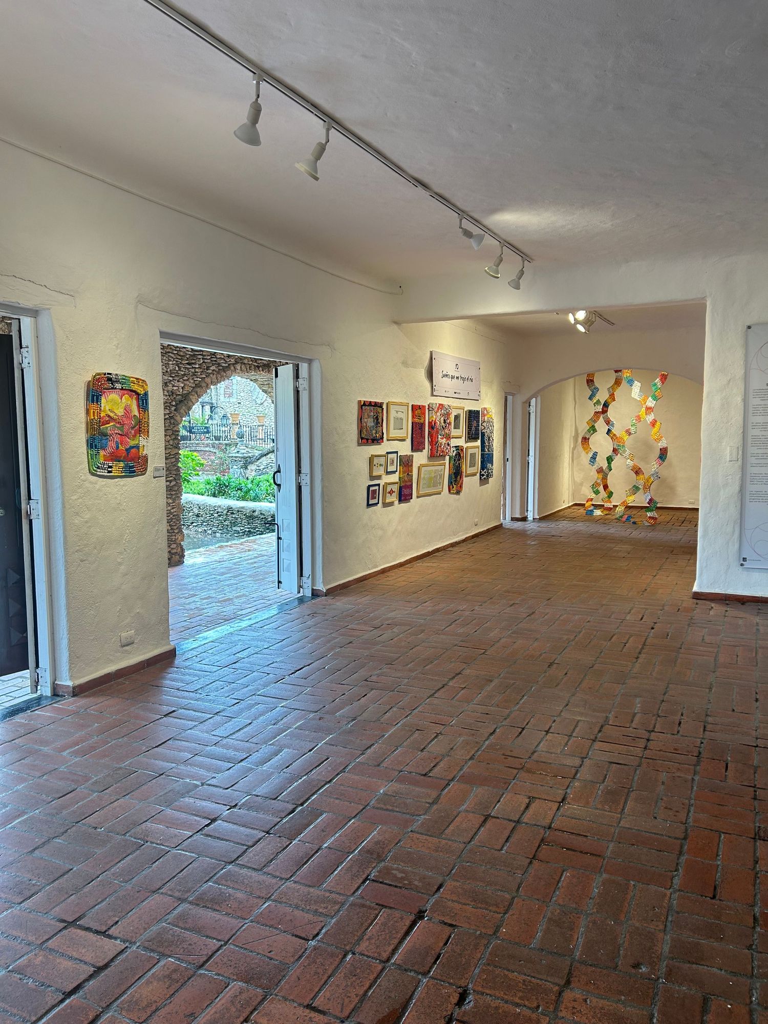 Gallery interior with track lighting, brick flooring, and various artworks displayed along white walls.