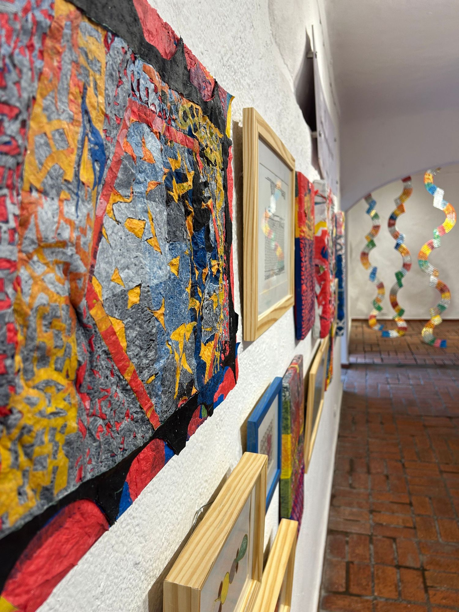 Close-up of textured abstract artwork on gallery wall with wooden frames visible.