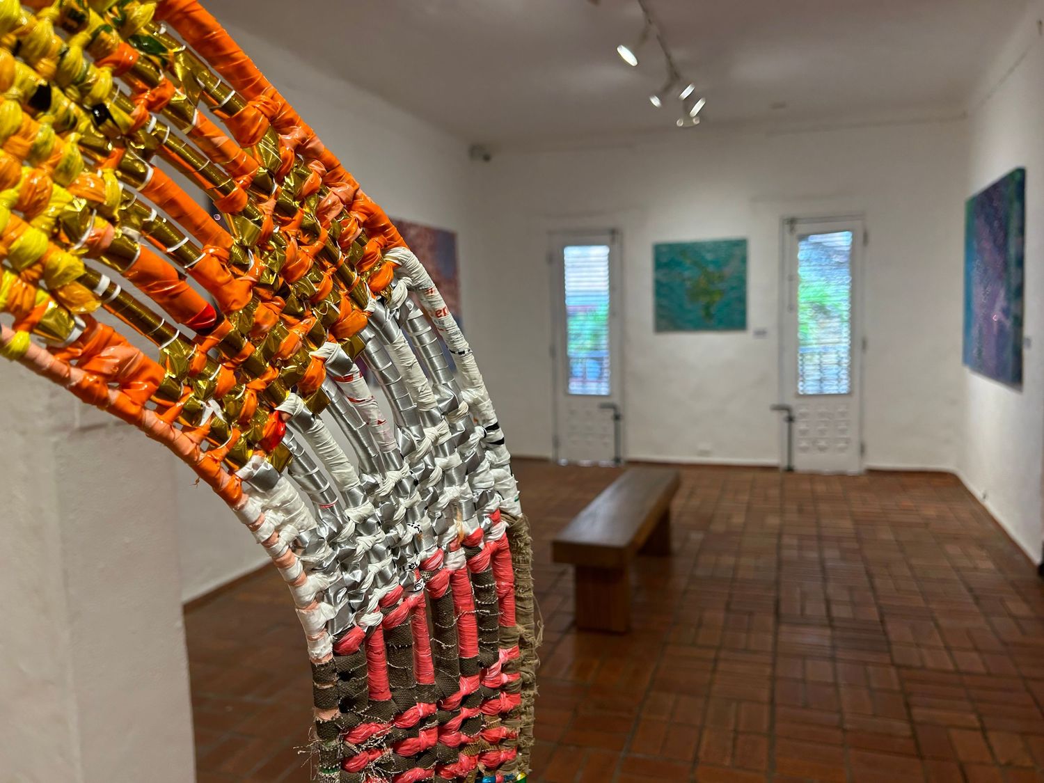 Art gallery interior with wood floors, white walls, and a vibrant curved sculptural installation.
