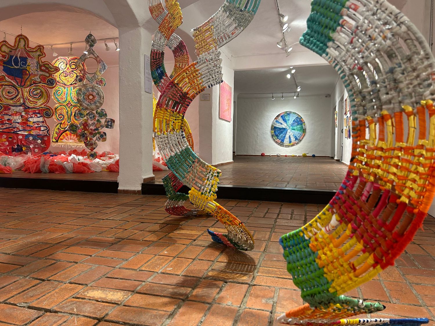 Colorful curved sculpture installation spanning across an art gallery with terracotta tile flooring.