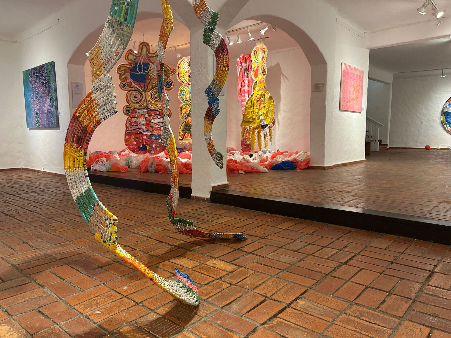 Modern art gallery with arched doorways and a colorful winding sculptural piece on the floor.