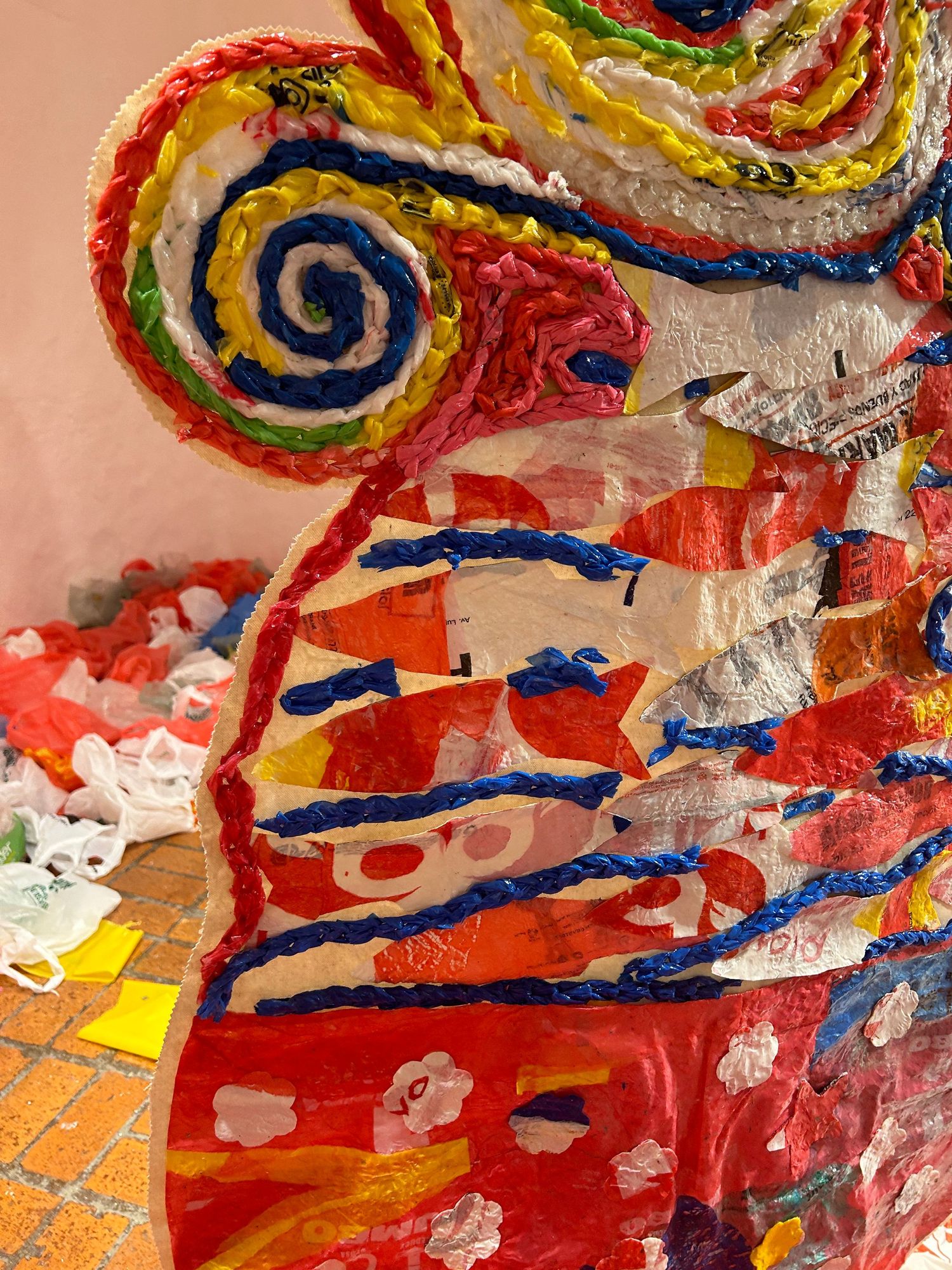Colorful spiral art installation with swirling patterns in red, yellow, and blue against a peach background.
