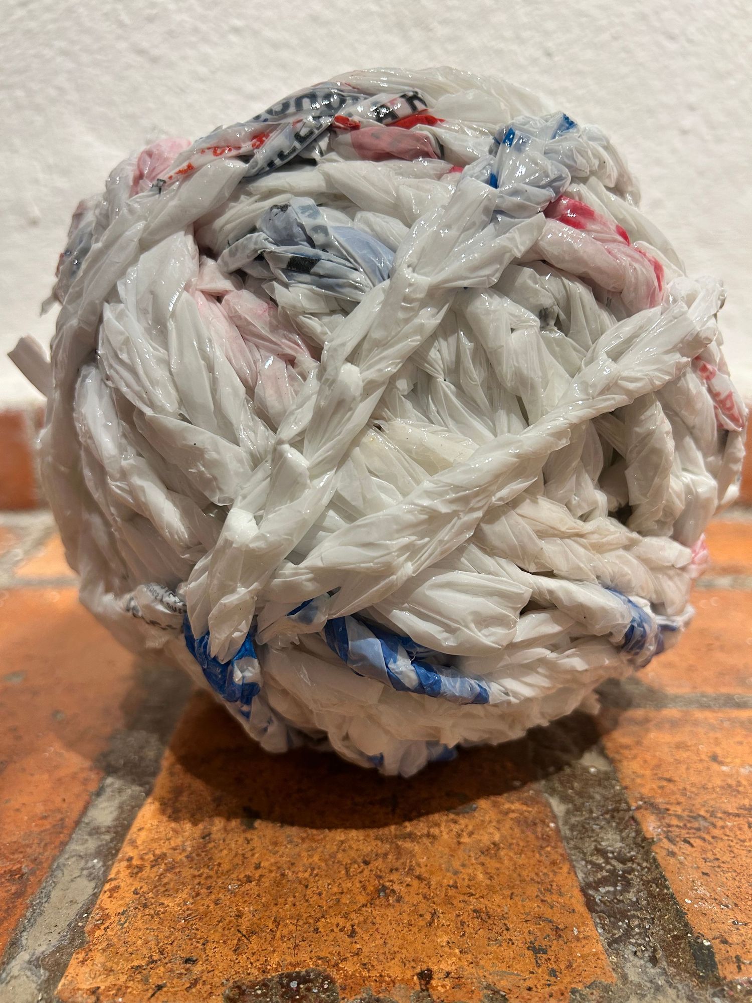Spherical sculpture made from crumpled white plastic bags with hints of red and blue.