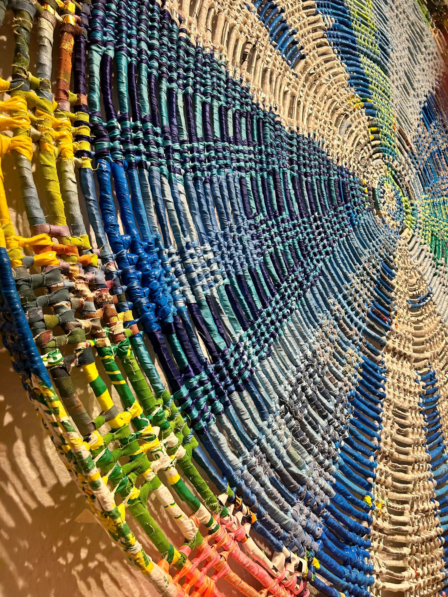 Close-up of a woven plastic artwork featuring concentric circles in vibrant blues, yellows, and greens.