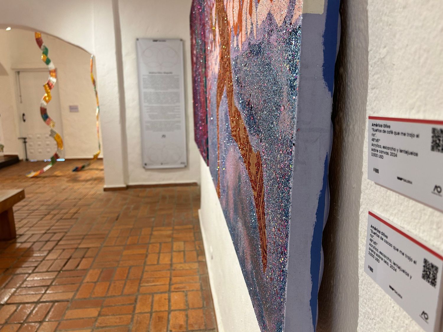 Art gallery hallway with terra cotta flooring showcasing colorful wall artwork and decorative panels.