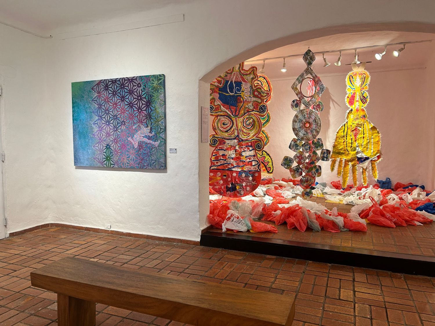 Gallery space with wooden bench and colorful art installations visible through archway.