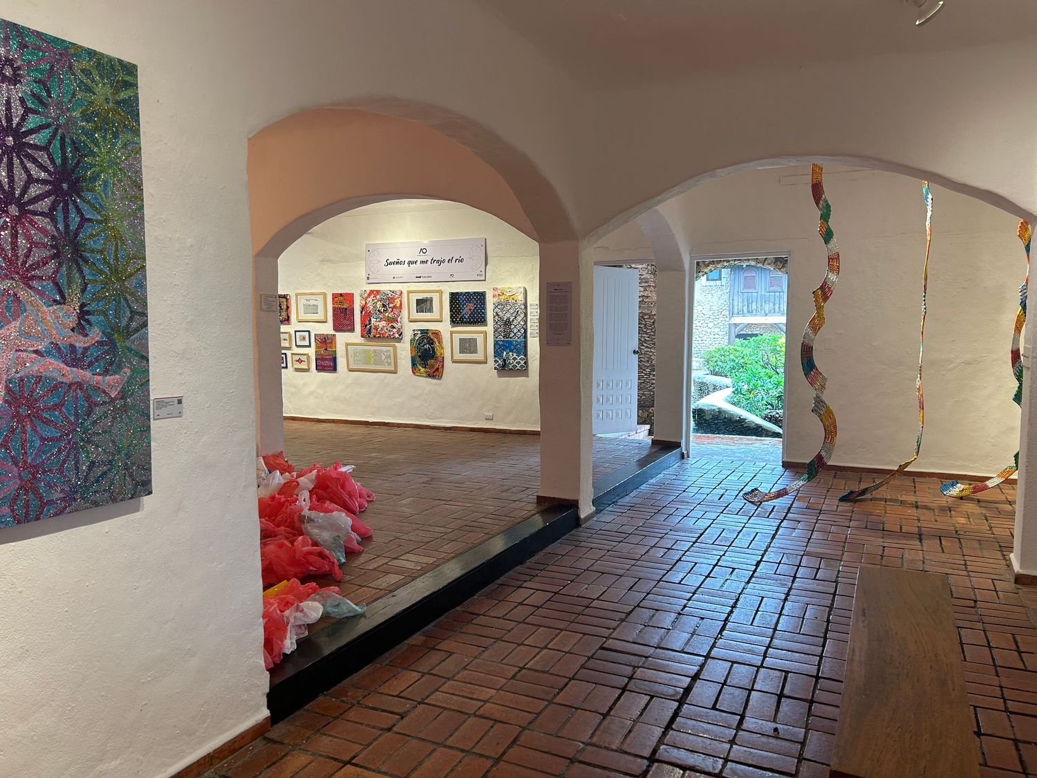 Art gallery hallway with arched doorways, terracotta floor, and vibrant wall displays.