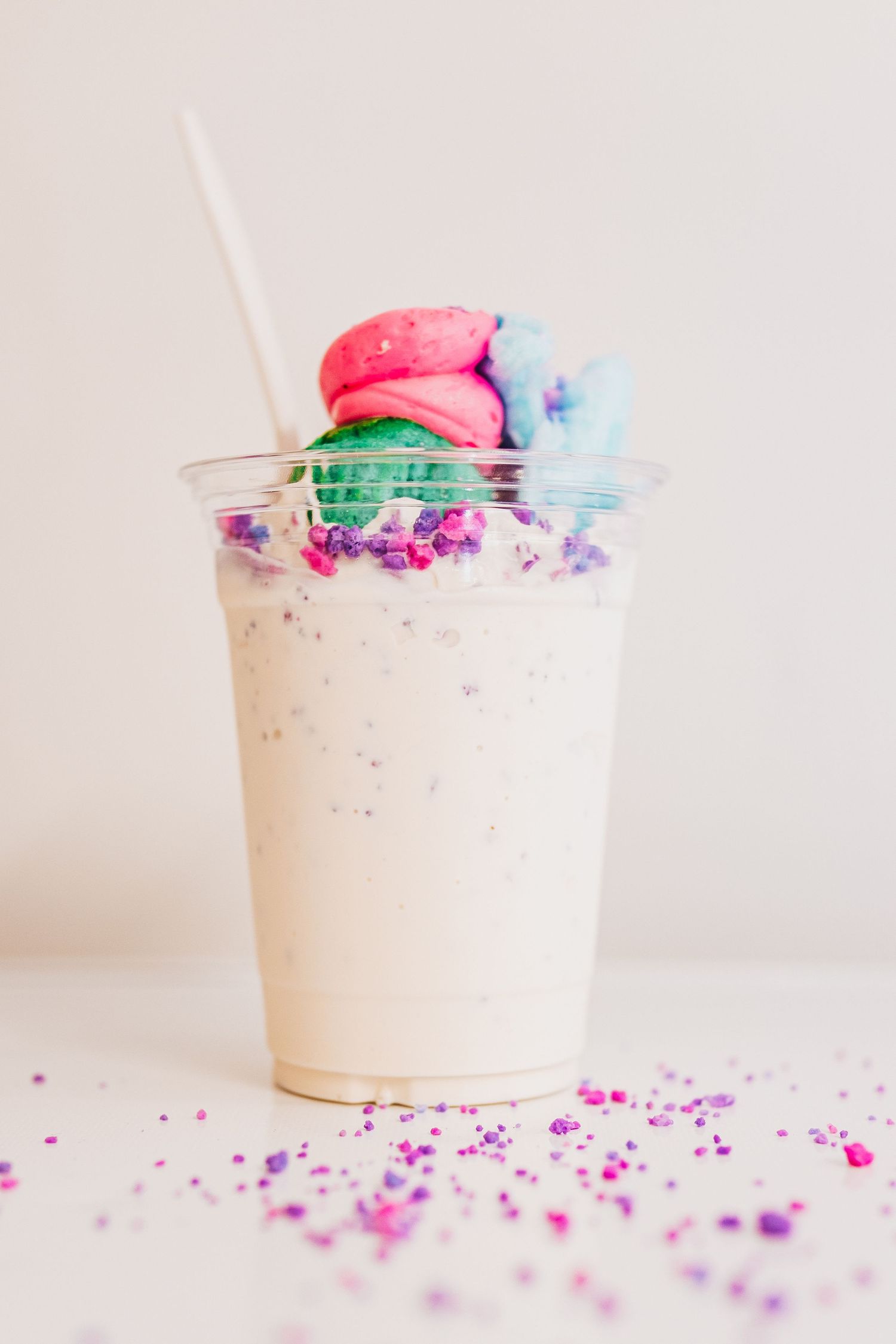 Whimsical milkshake topped with colorful macarons and sprinkles scattered on white surface.
