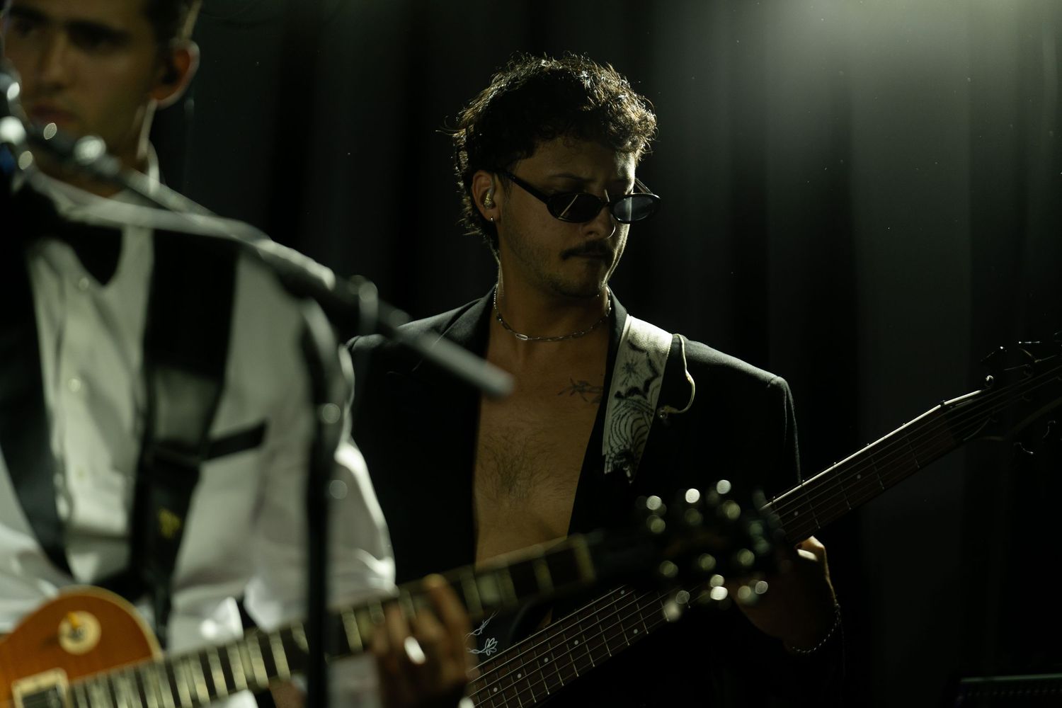 Band members perform on stage during a dark, moody concert with dramatic lighting.
