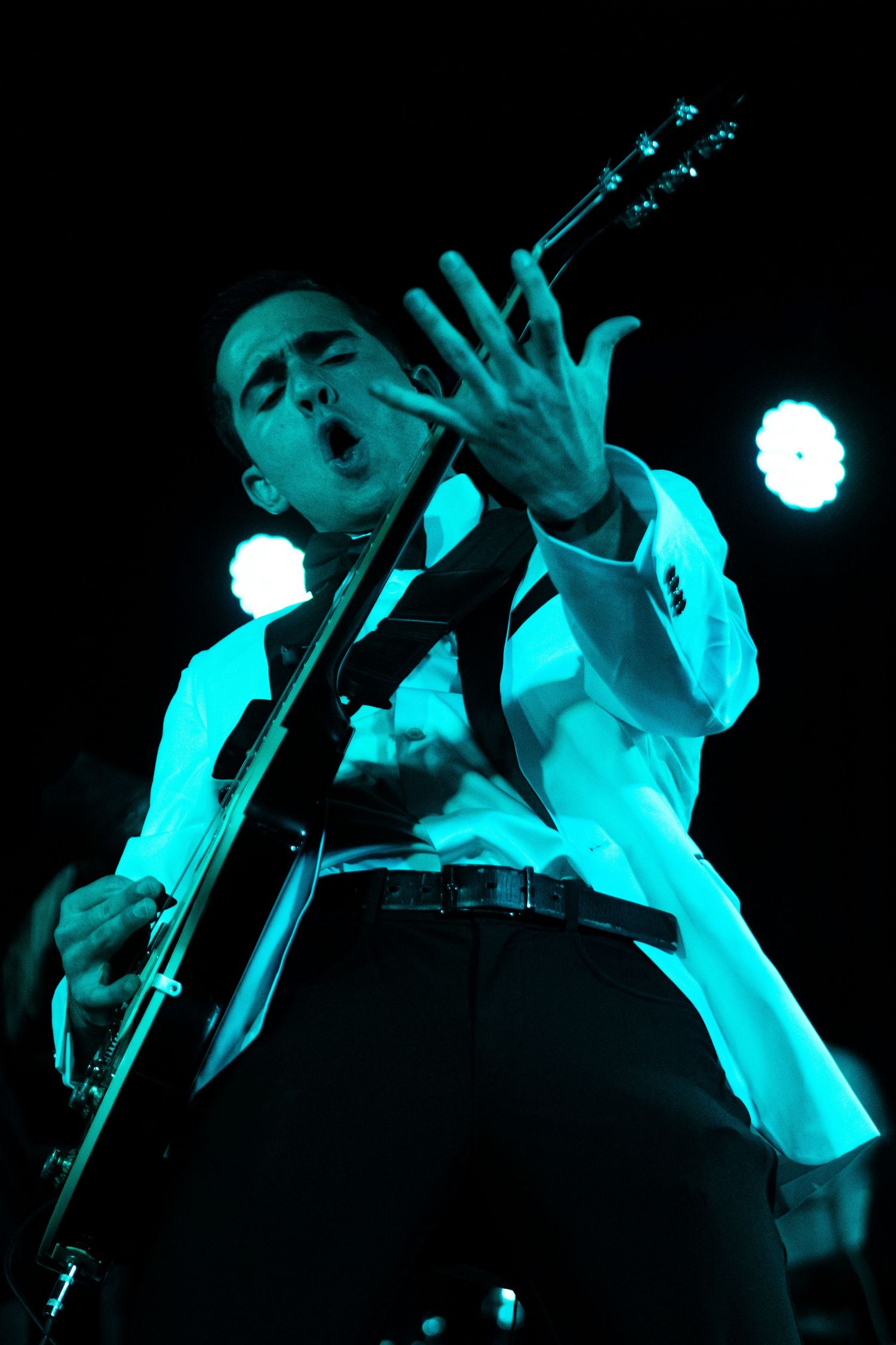 Musicians perform on stage bathed in dramatic turquoise lighting with silhouetted figures creating a haunting atmosphere.