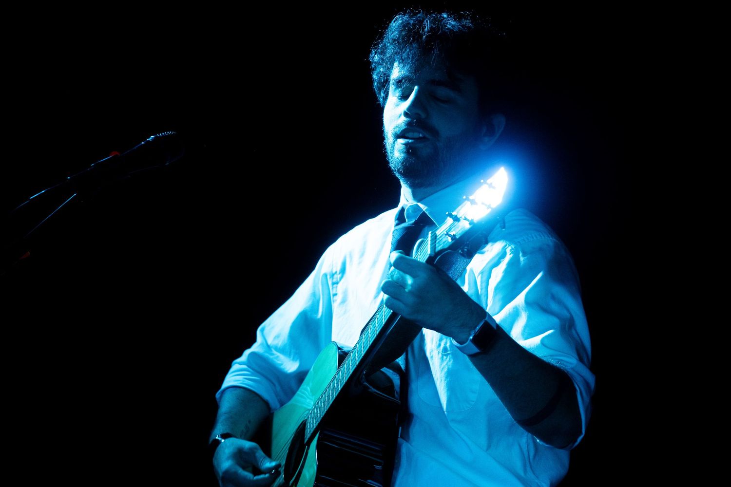 Professional performer sings passionately on stage in dramatic blue lighting during live concert performance.