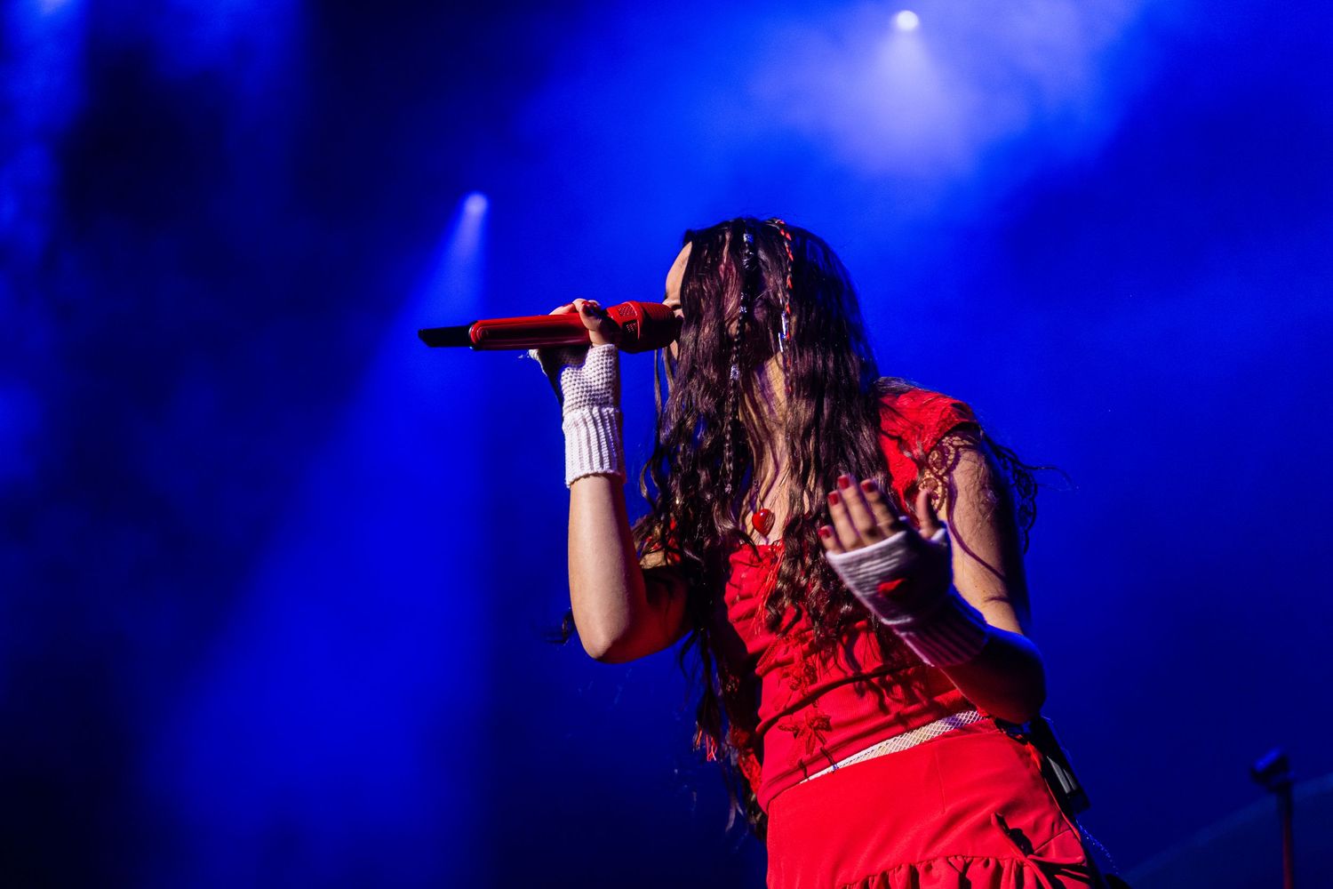 Joaquina in a red outfit sings on stage illuminated by dramatic blue lighting during a concert performance.