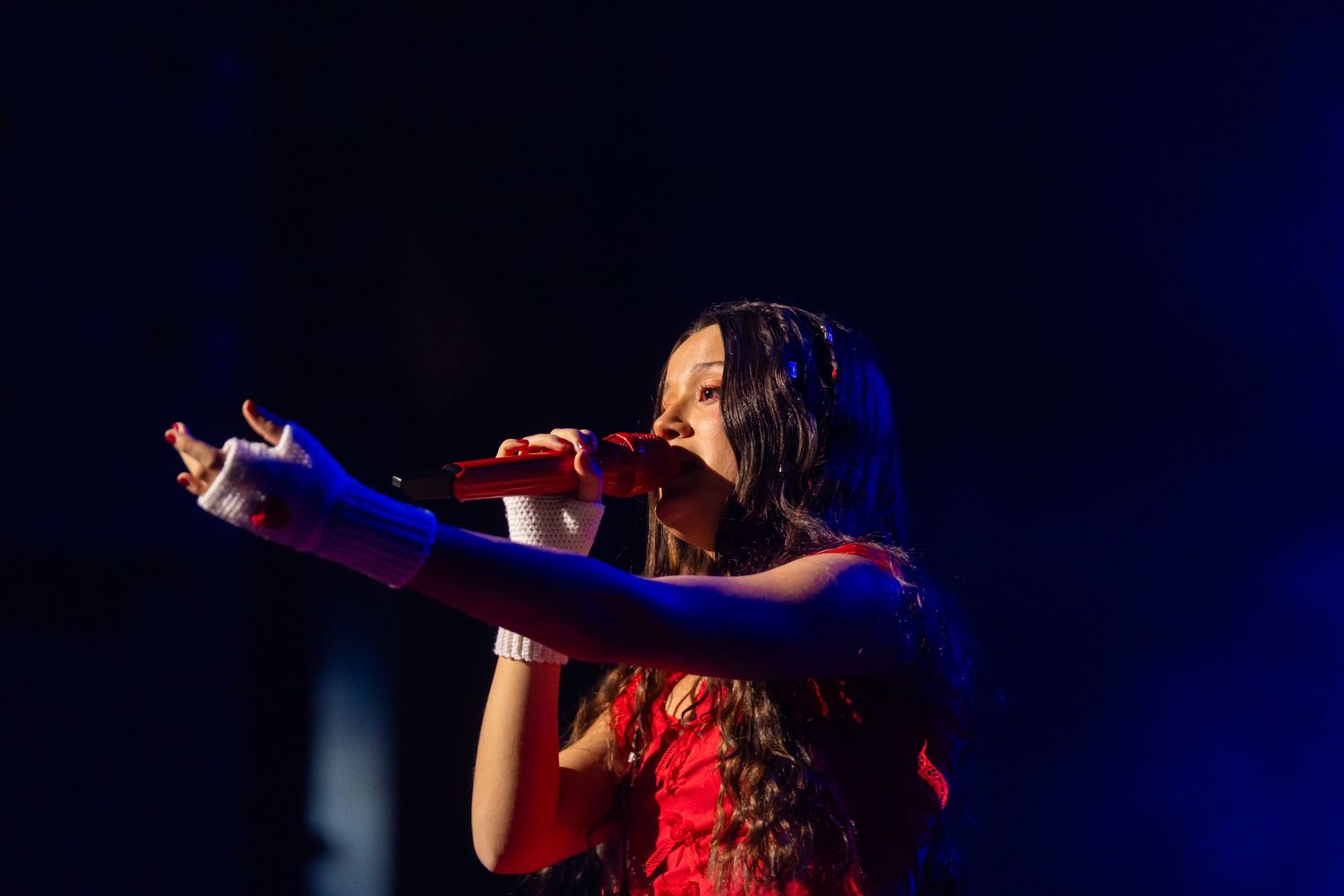 Joaquina in a red dress performs passionately on stage under dramatic blue lighting during a concert performance.