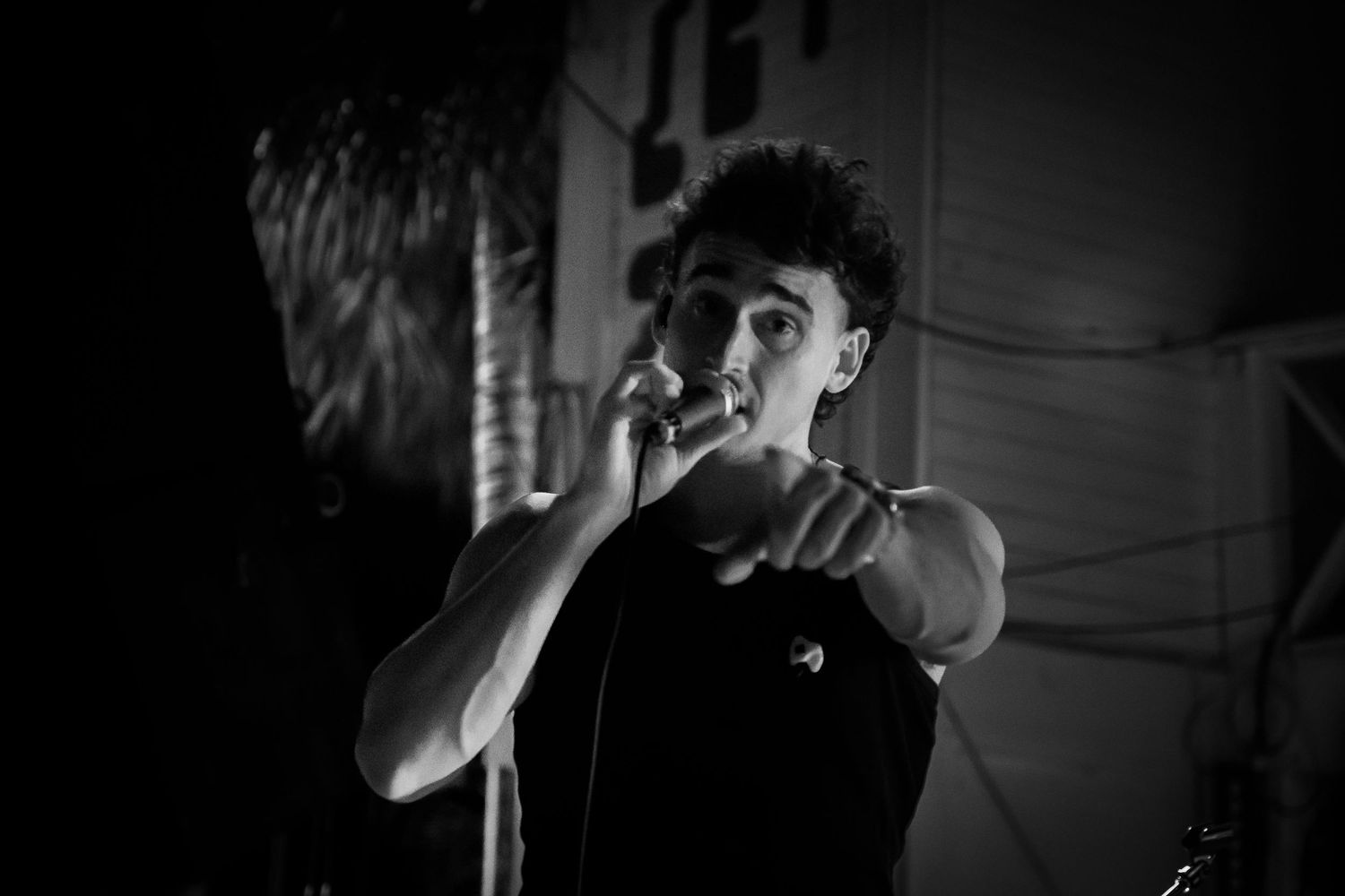 A performer sings passionately into a microphone during a black and white performance shot on stage.