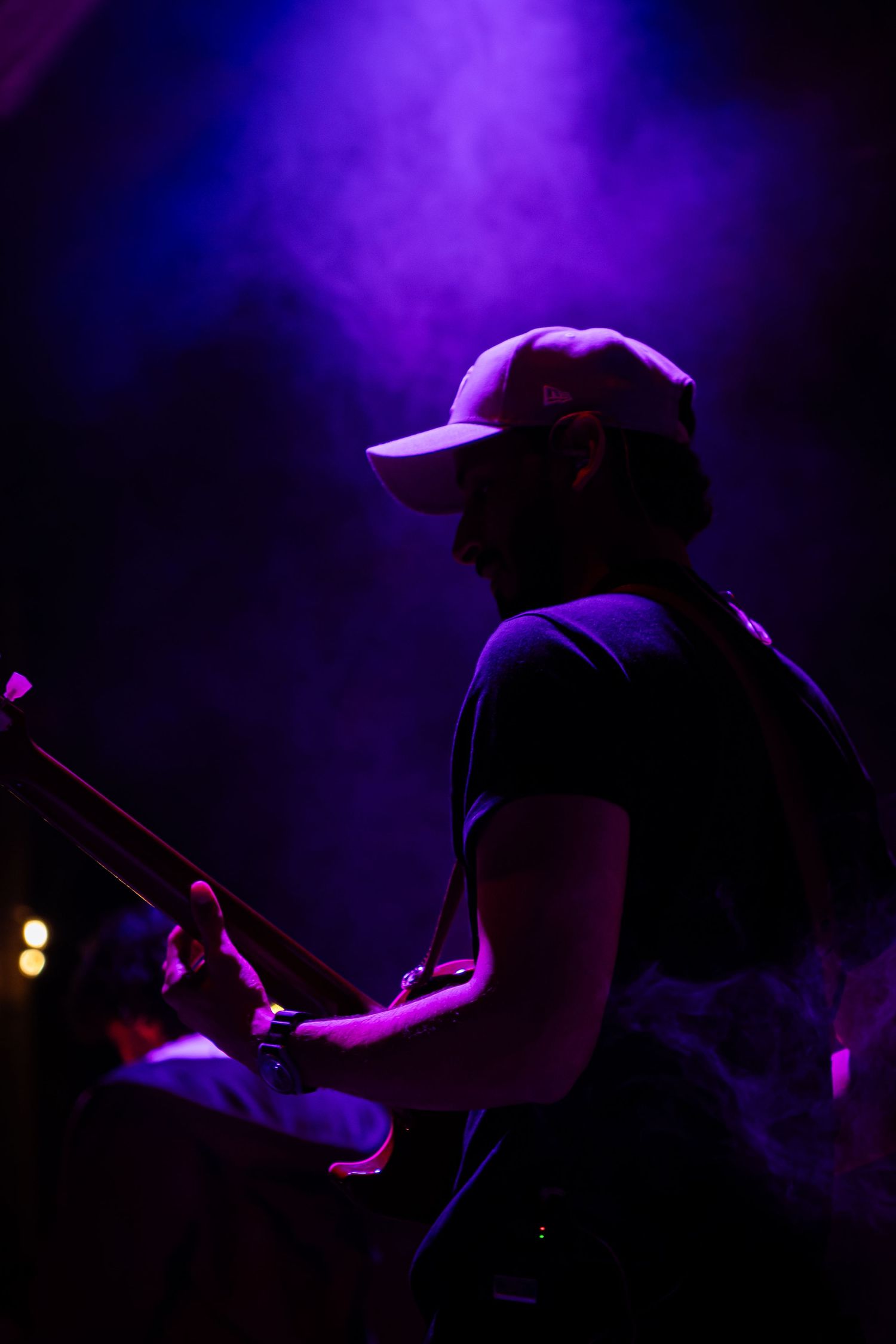 Silhouetted drummer performs on stage surrounded by purple and blue atmospheric lighting during concert.