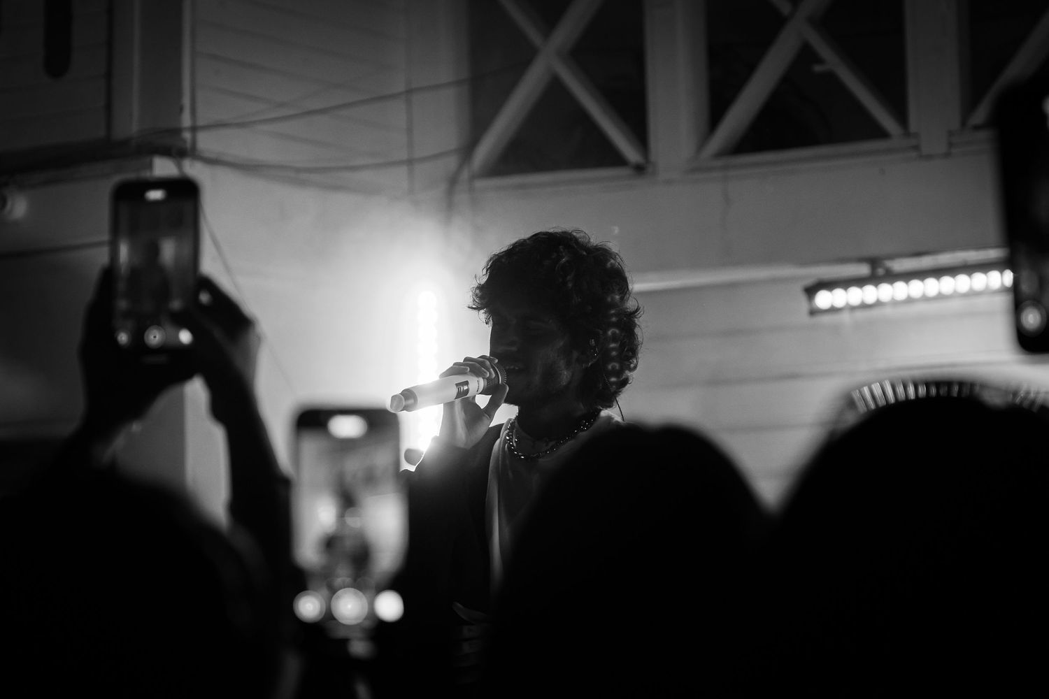 Black and white concert photo showing a silhouetted performer on stage with a microphone.