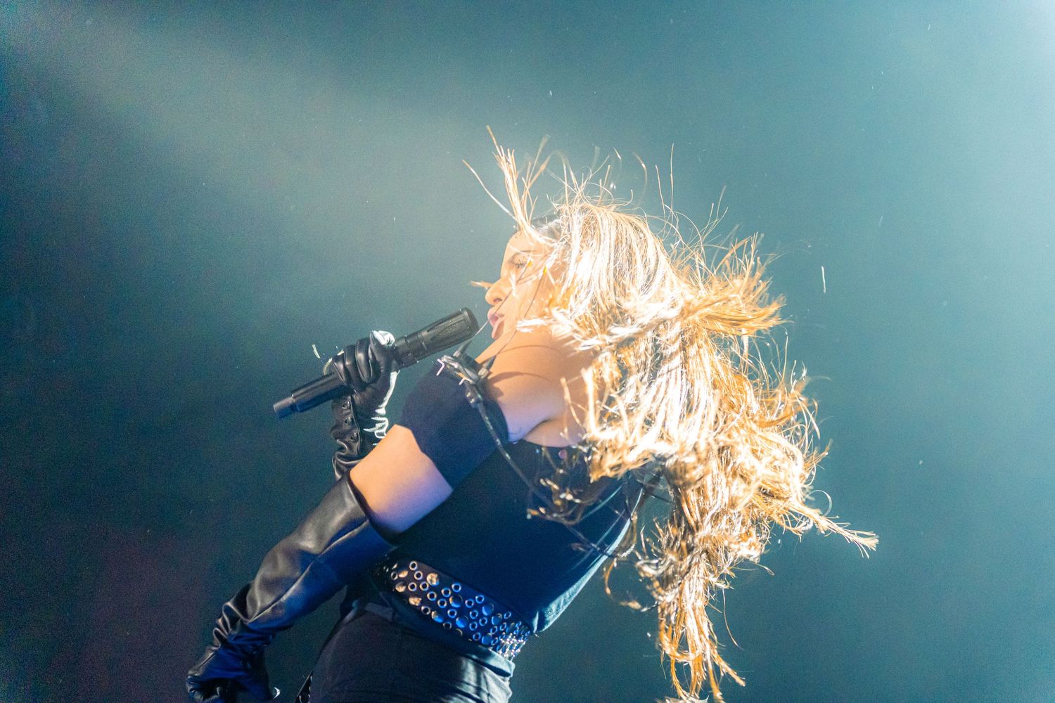 Energetic Nathy Peluso with blonde hair in motion while singing against blue-tinted concert lighting.
