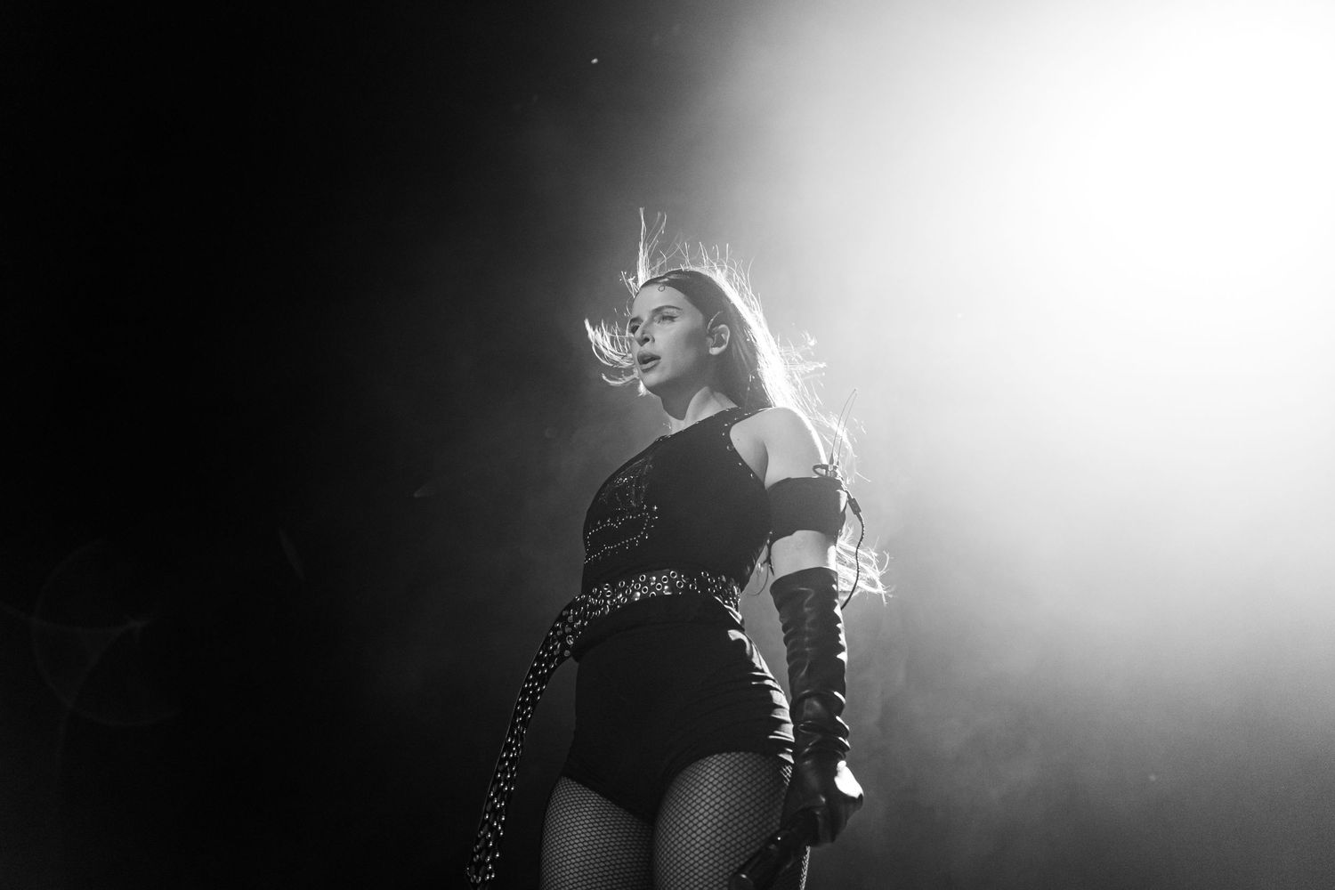 Nathy Peluso in a black leotard stands on stage in dramatic lighting with smoke effects during a concert performance.