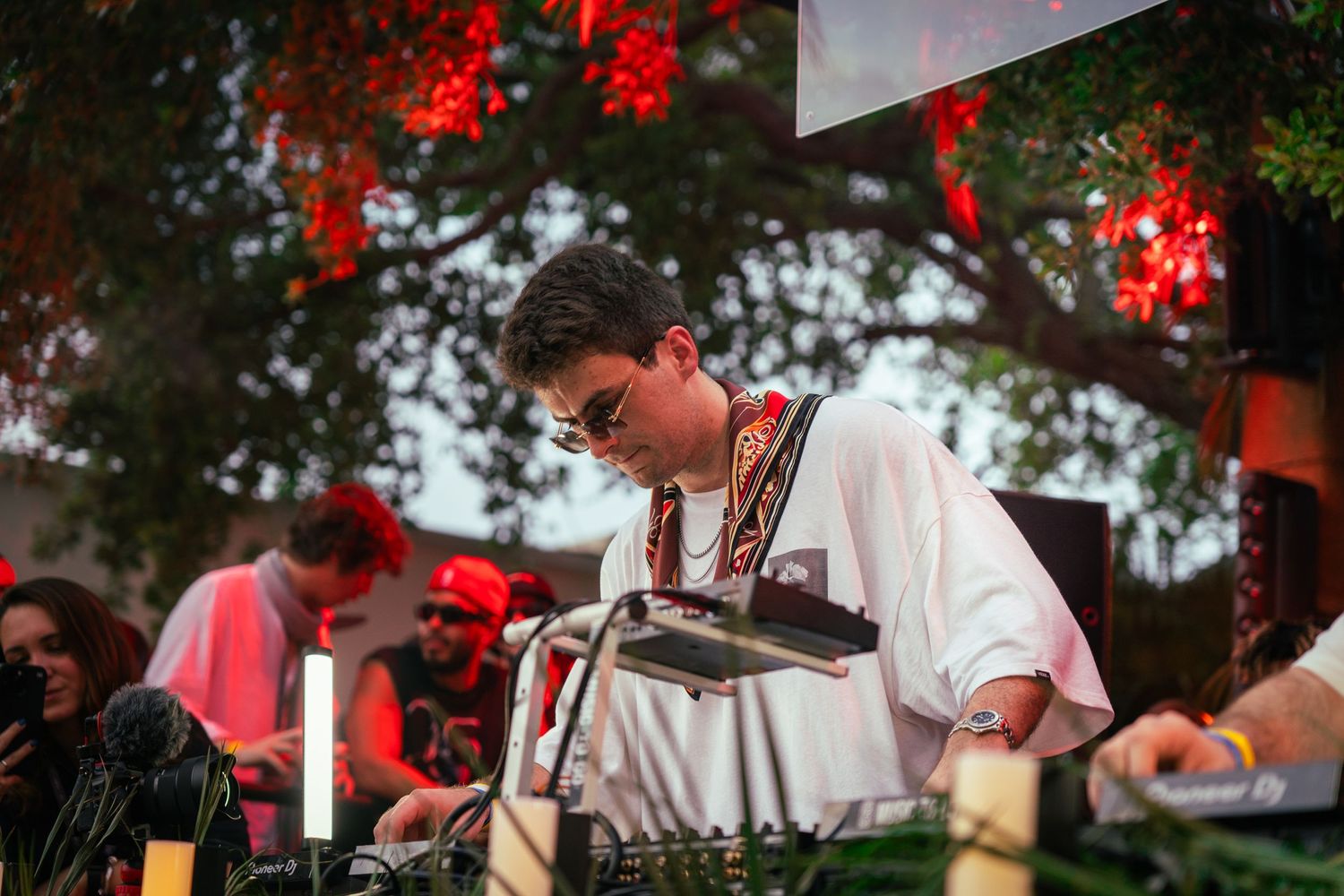 DJ performs at outdoor event with red lighting and equipment setup.