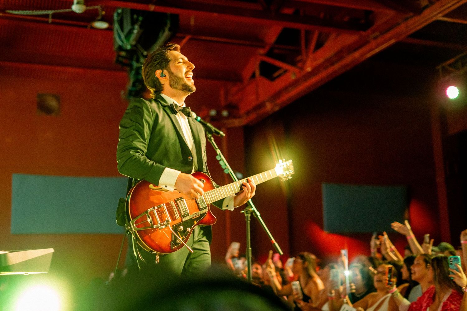 Agustín Zubillaga. Live concert performance with guitarist playing on stage under red lighting.