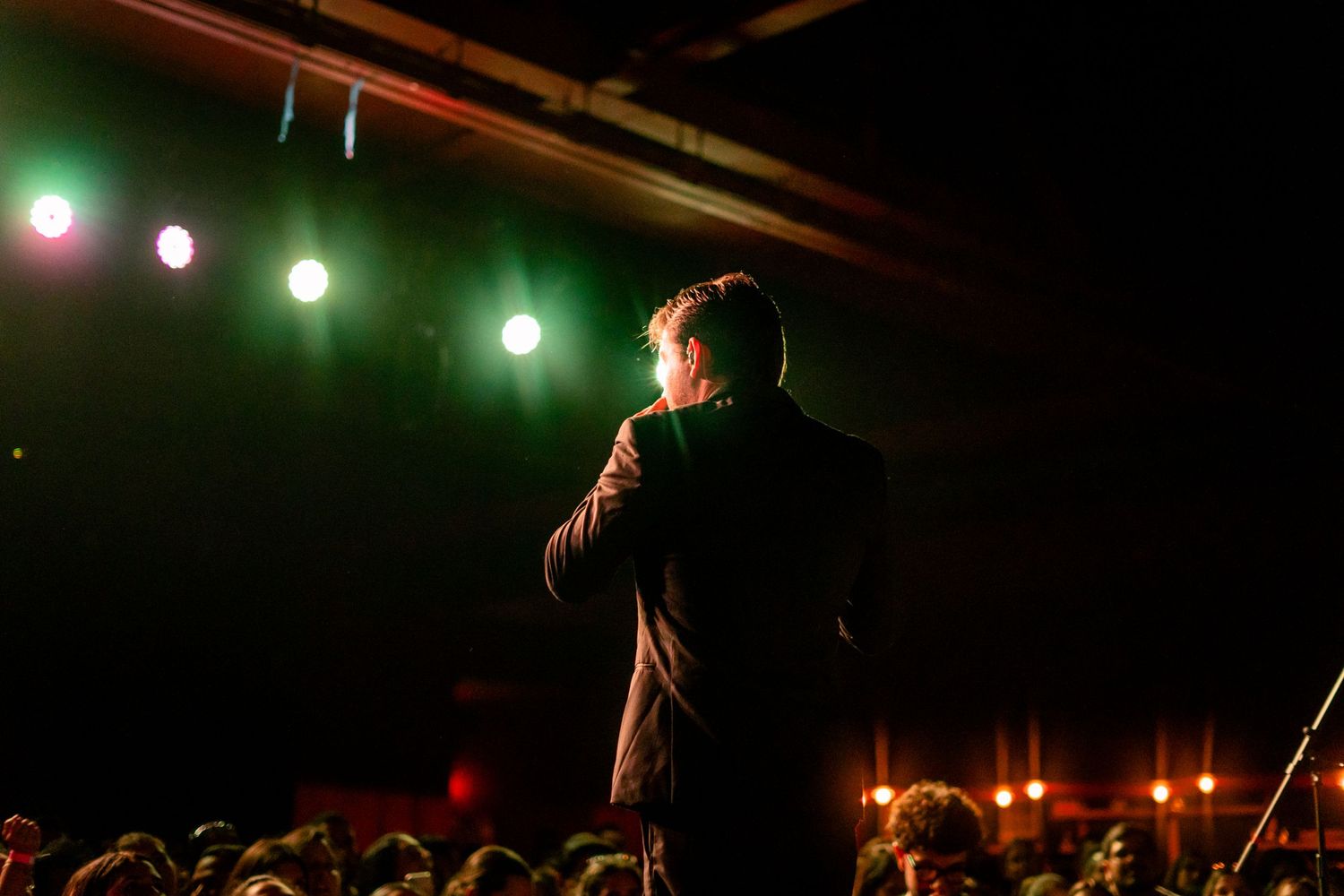 Luis Jiménez. Silhouette of a performer on stage with green spotlights illuminating the dark background.