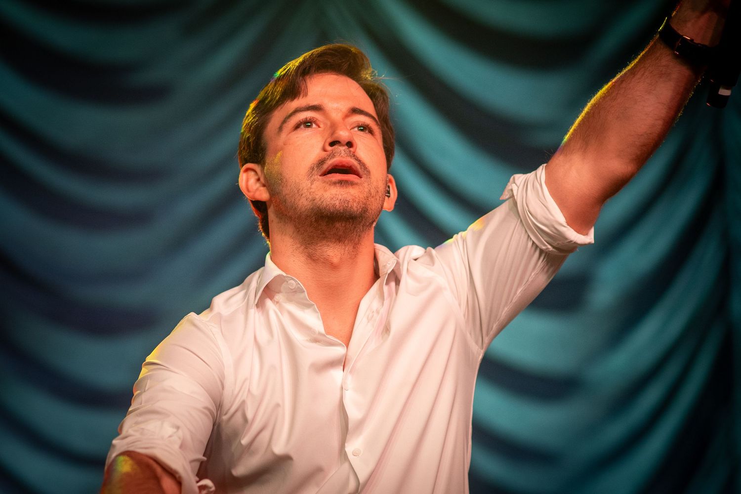 Luis Jiménez. Dramatic performance moment captured against teal curtain backdrop with stage lighting.
