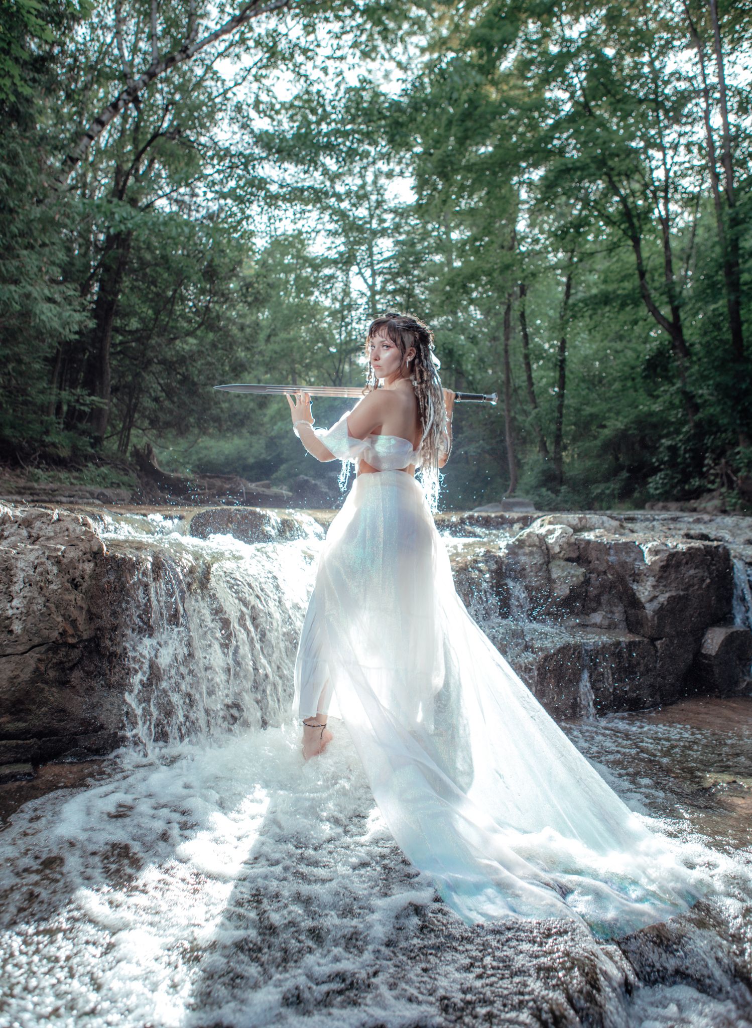 Ethereal bridal portrait at a cascading waterfall with flowing white dress catching the light.