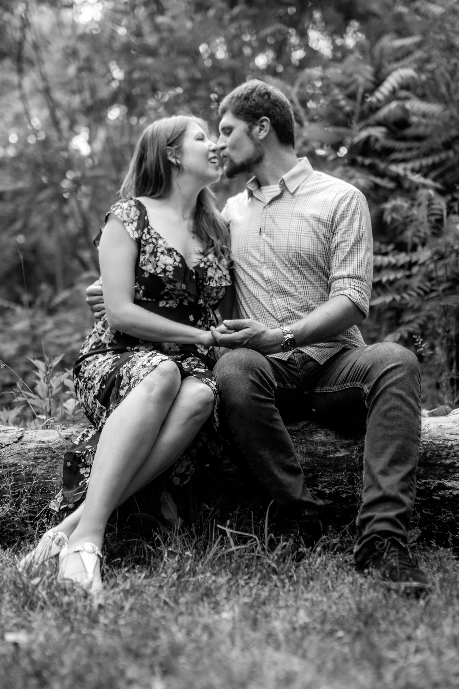 Black and white photo of couple sitting intimately together on grass.