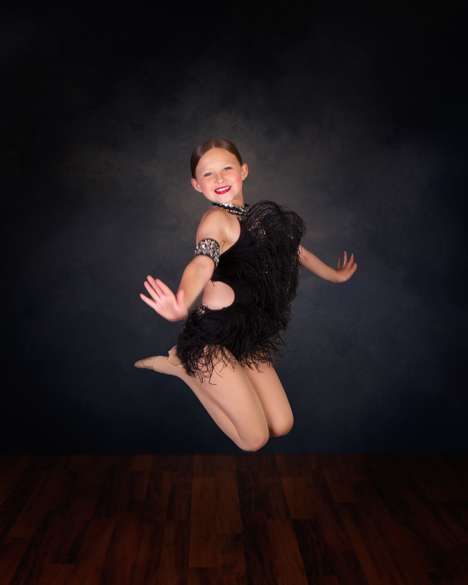A dancer in a black feathered costume leaps gracefully against a dark studio background.