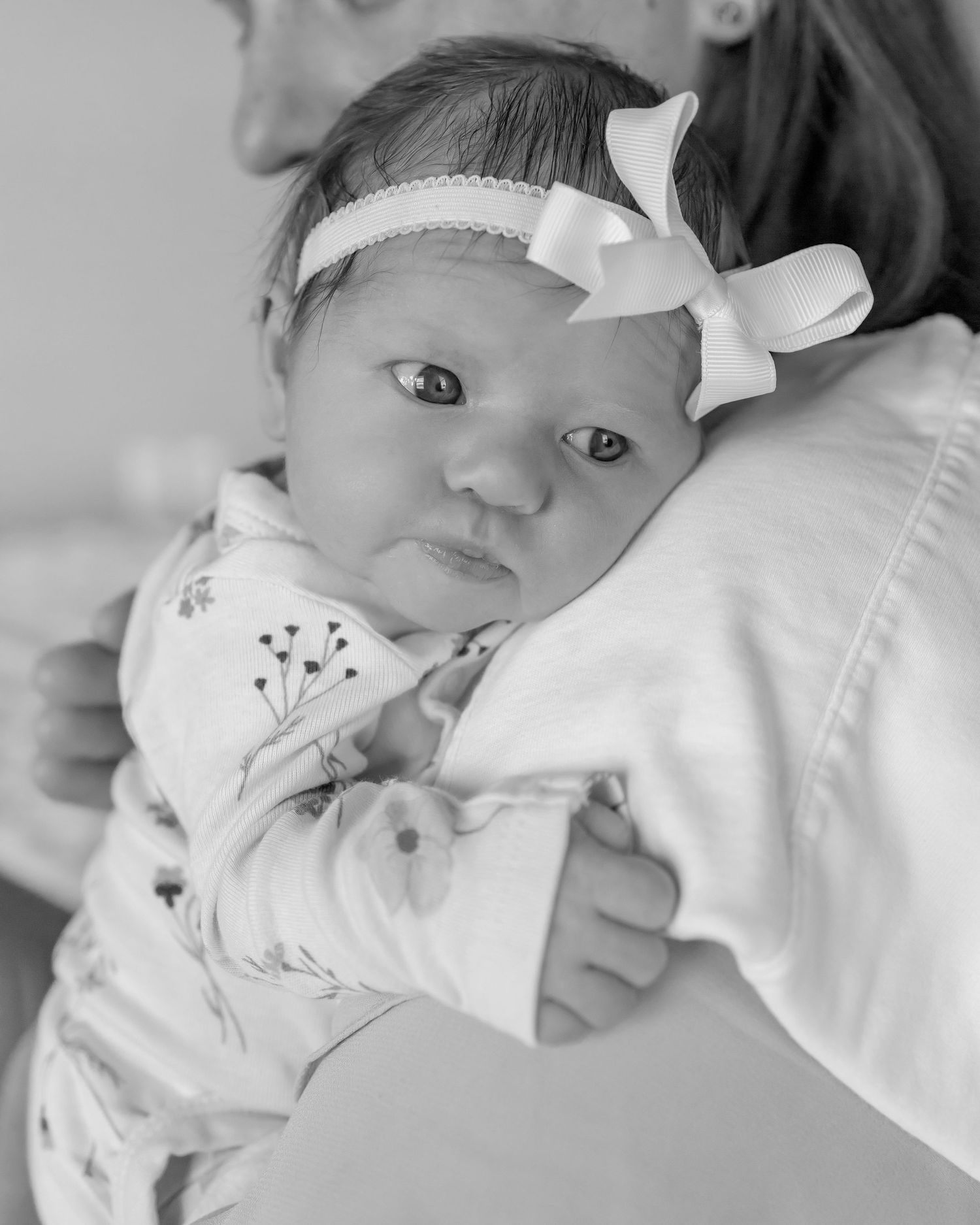 black and white close up of a newborn held on mothers chest, babys head on mothers shoulder, she is wearing a white bow
