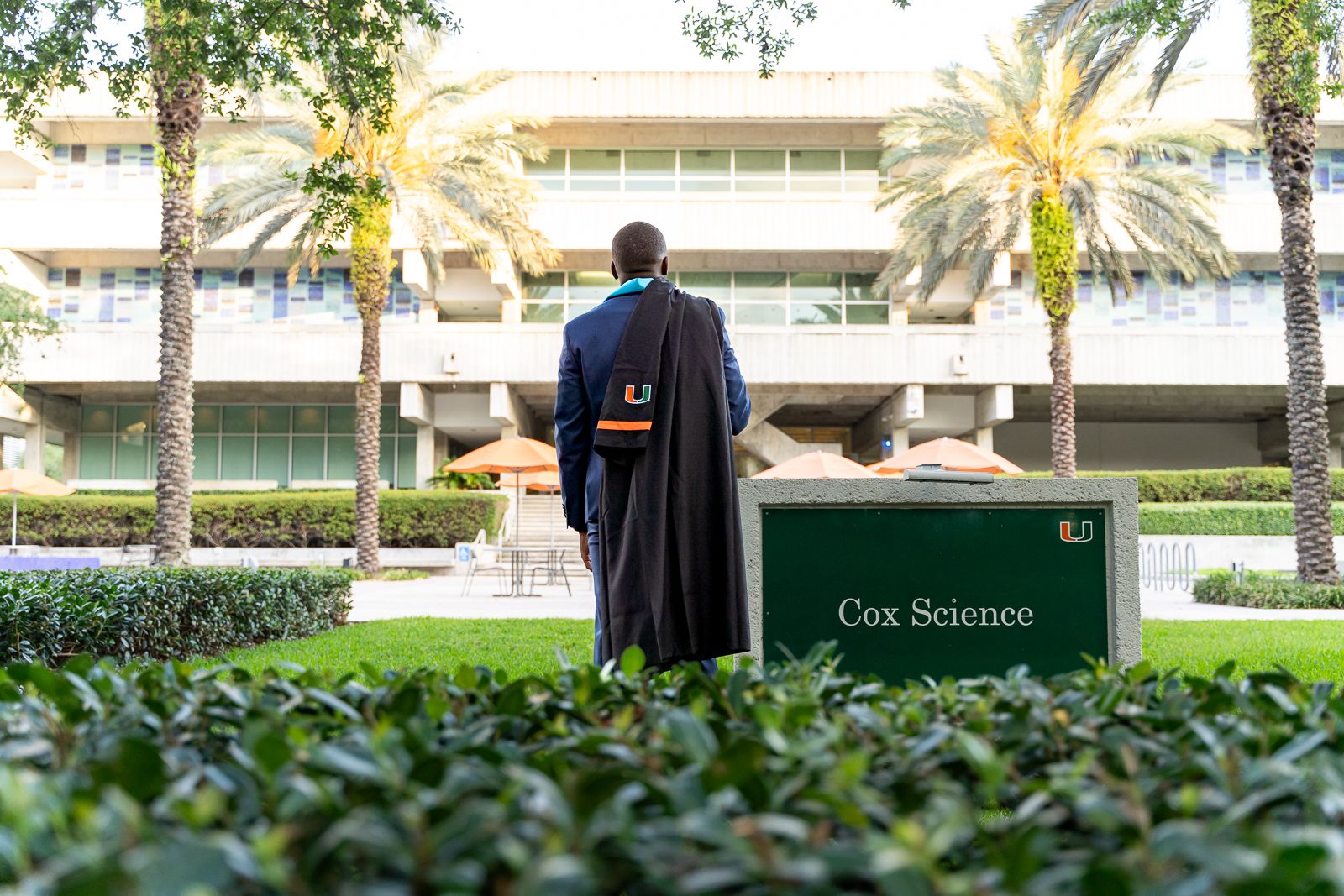Graduate in cap and gown standing in front of modern campus building.