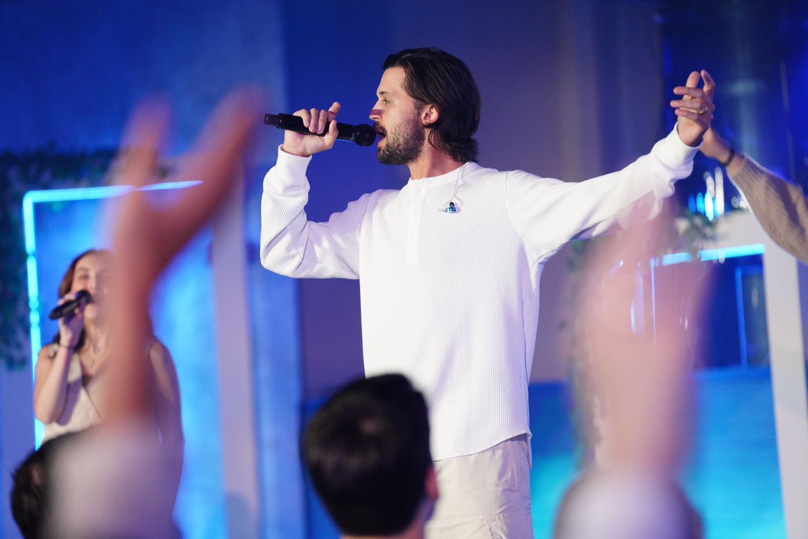 Performer singing on stage with microphone under blue lighting.