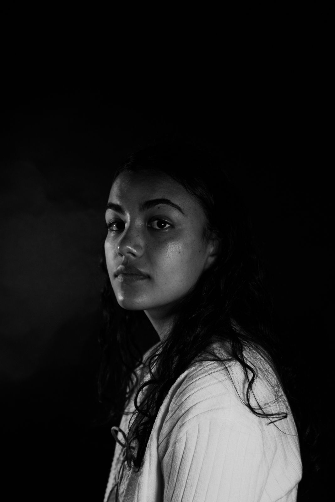 Dramatic black and white portrait with moody lighting against dark background.