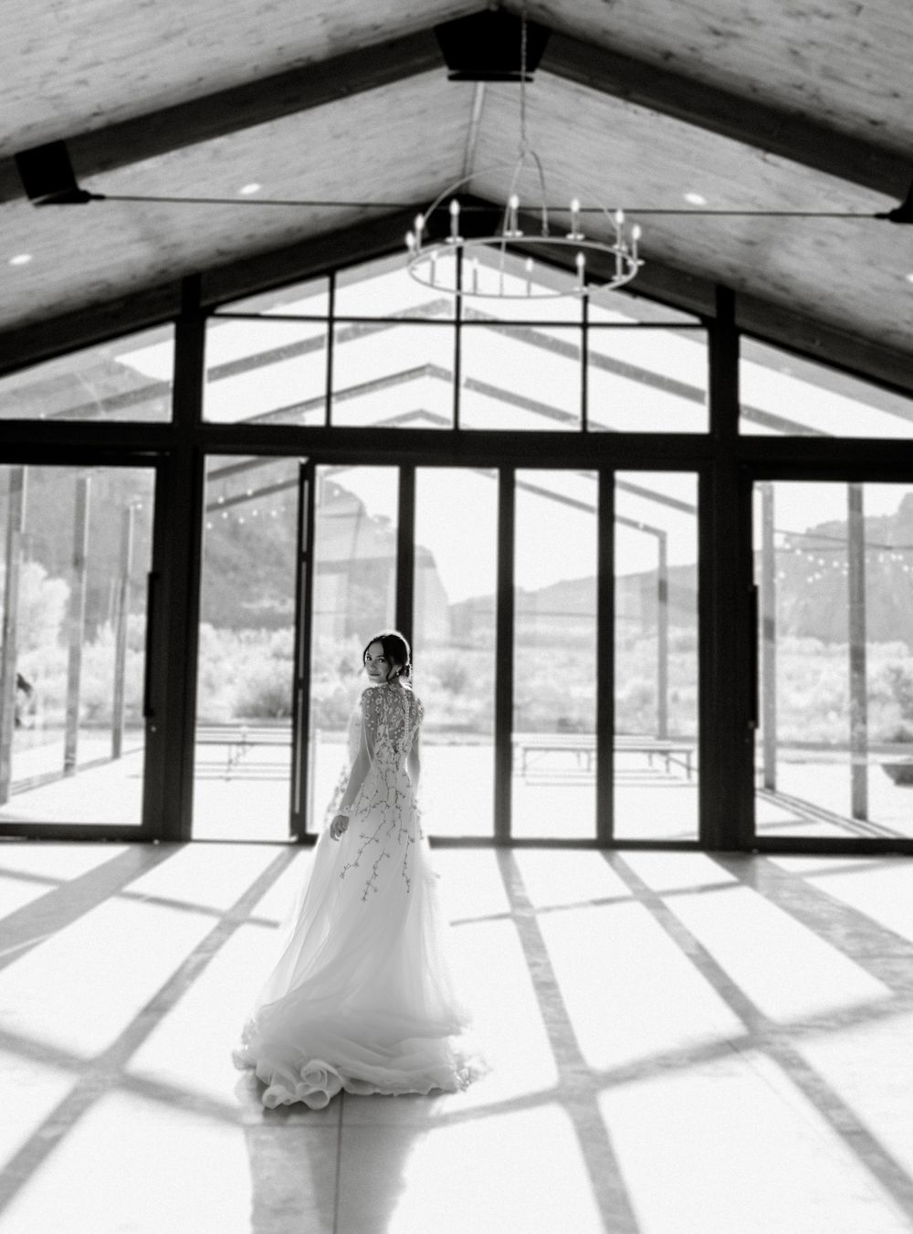 A white wedding gown silhouette stands in dramatic lighting inside a modern glass-walled venue.