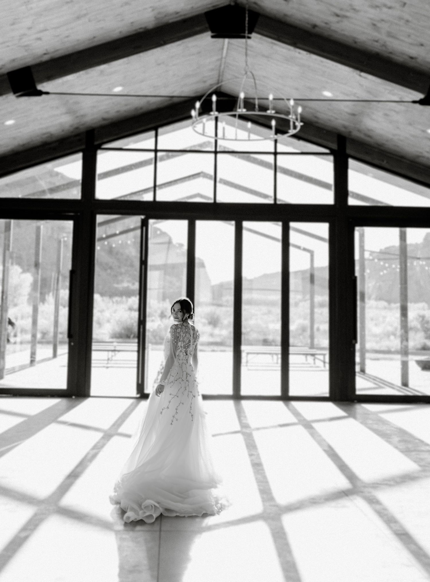 A white wedding gown silhouette stands in dramatic lighting inside a modern glass-walled venue.
