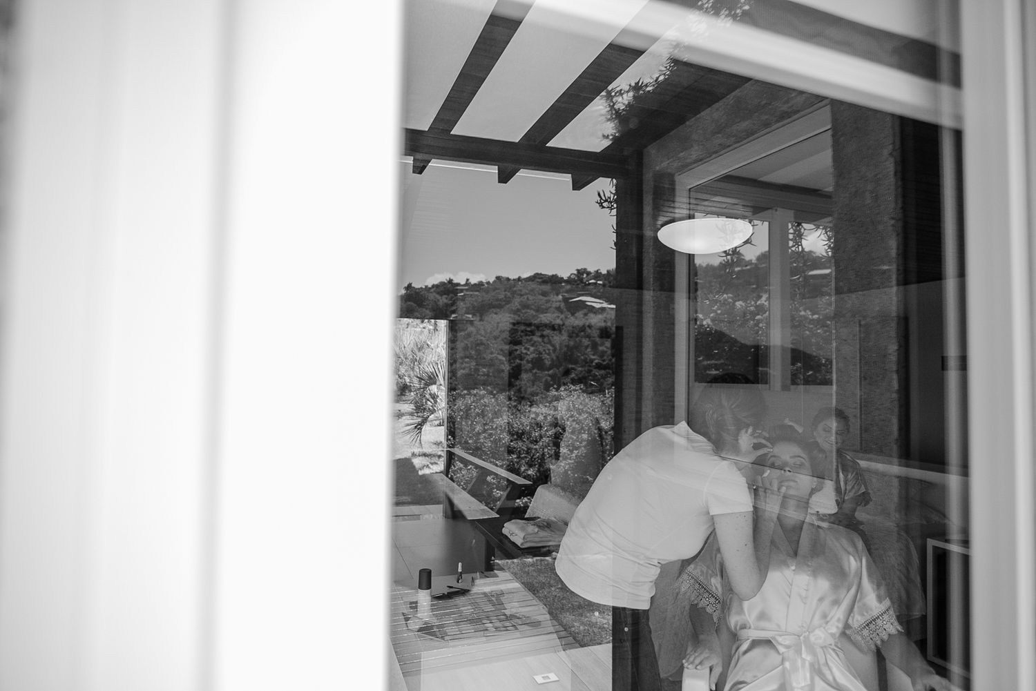 A black and white view through a window showing intimate indoor moments.