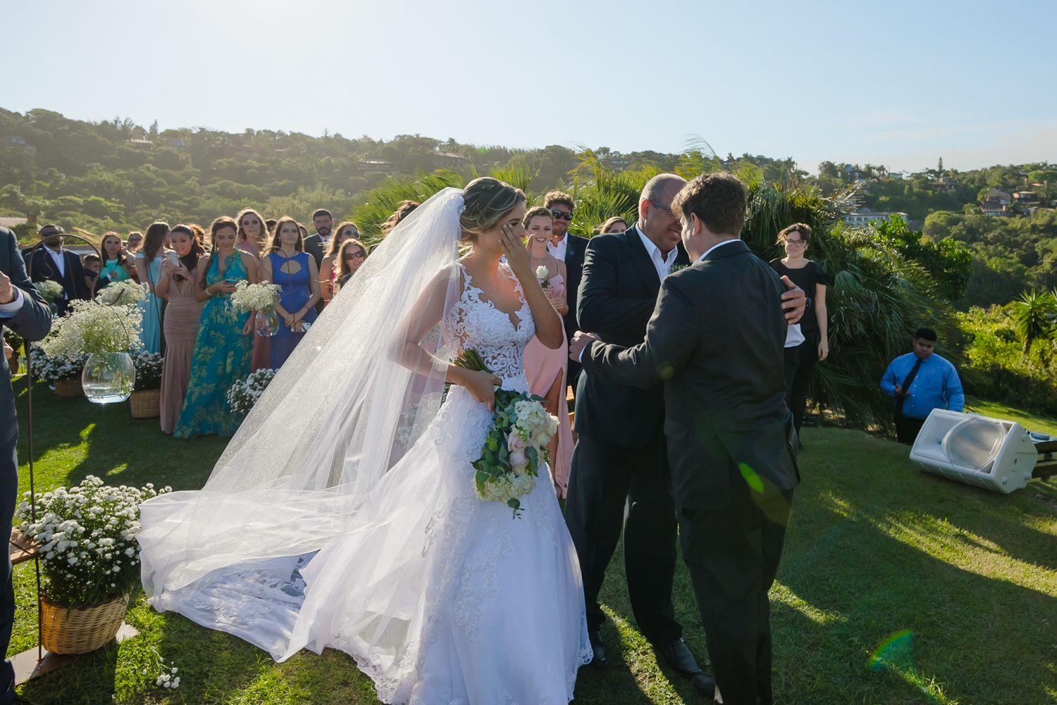 Outdoor wedding ceremony taking place on a hilltop with guests watching the vows being exchanged under blue skies.