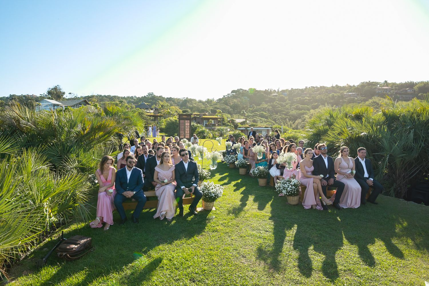 Scenic hillside wedding ceremony with guests seated on the lush green lawn under blue skies.