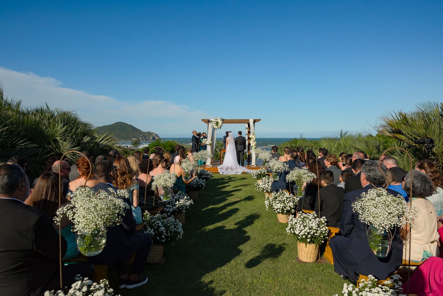 Beautiful outdoor wedding aisle decorated with white floral arrangements leading to a wooden arch.