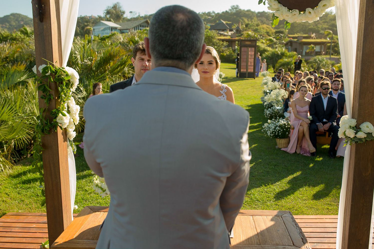 Wedding officiant addresses gathered guests from wooden platform during outdoor ceremony.