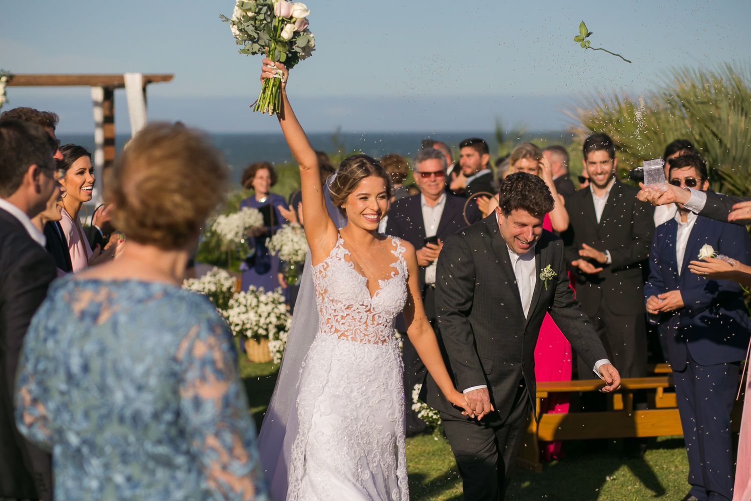 Celebratory moment during an outdoor wedding ceremony with ocean views and decorated wooden pergola.