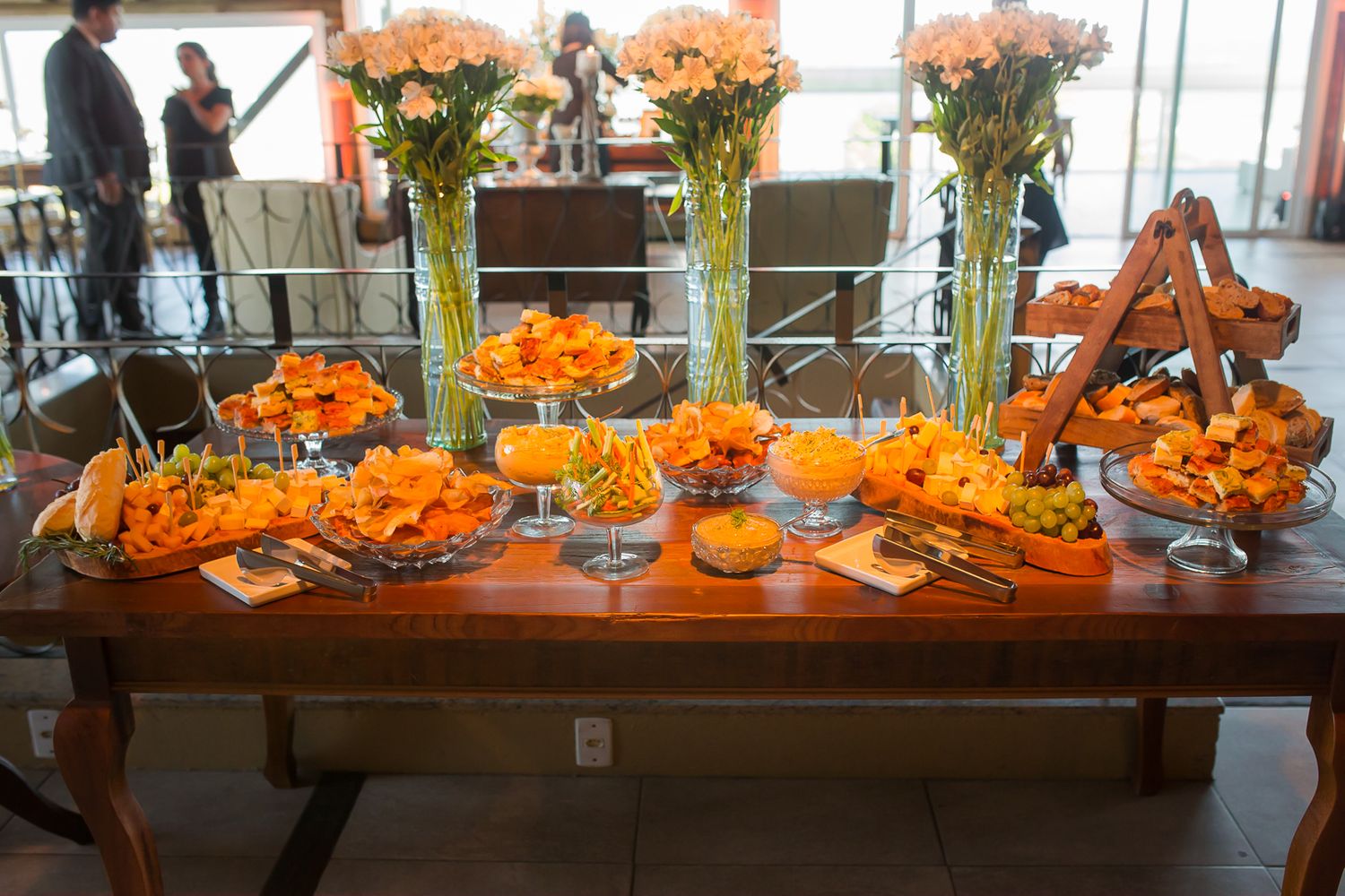 Long wooden table decorated with orange flowers and tall glass vases for wedding reception.
