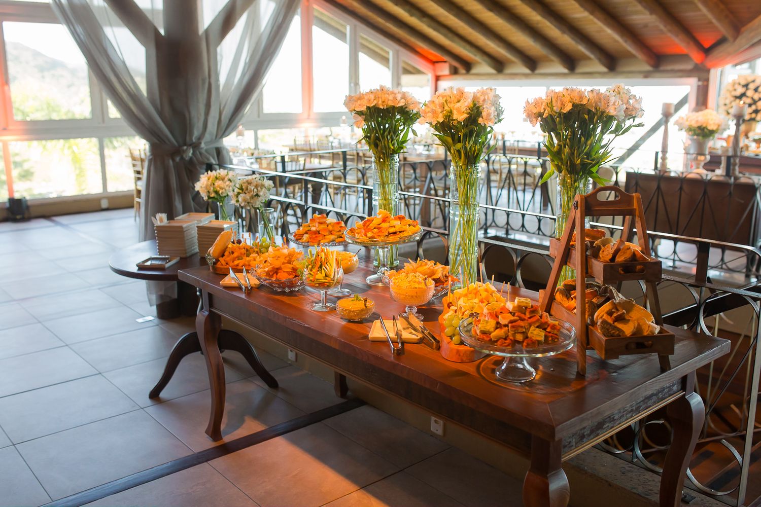 Reception table adorned with orange floral arrangements and tall glass vases in rustic indoor venue.